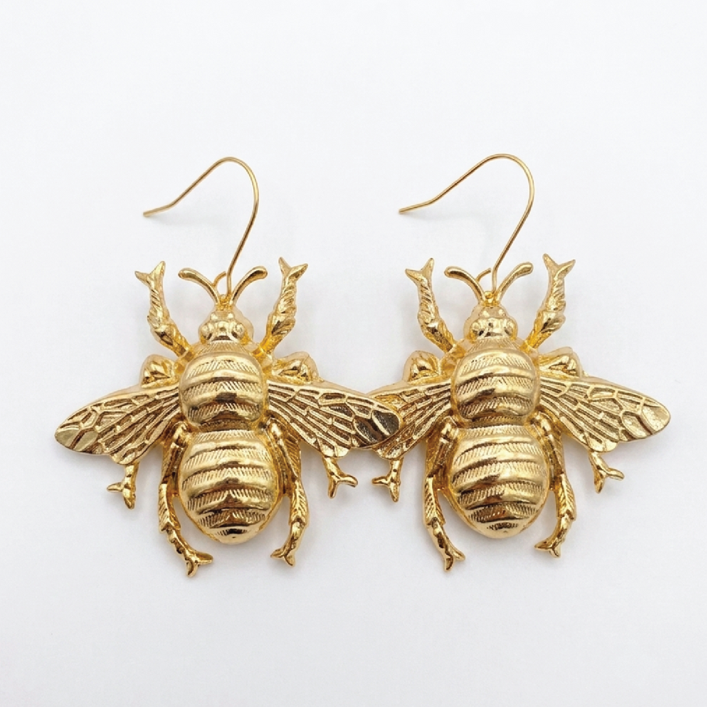 A pair of gold bee-shaped dangle earrings with textured wings and hooks, displayed on a clean white background.