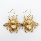 A pair of gold bee-shaped dangle earrings with textured wings and hooks, displayed on a clean white background.