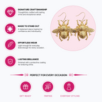 Gold bee-shaped drop earrings displayed on a light pink circular background with marketing text and icons about craftsmanship, stand-out appeal, effortless wear, and lasting shine.